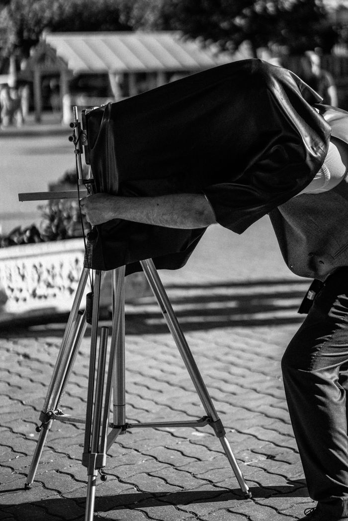 Black and white photograph of a vintage photographer working outdoors with a large-format camera.